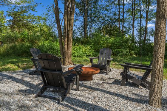 Fire pit and chairs on a gravel pad under the trees.